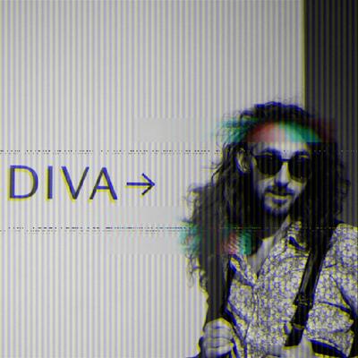 A bearded man with long hair stands in front of a sign that reads DIVA. He is wearing sunglasses.